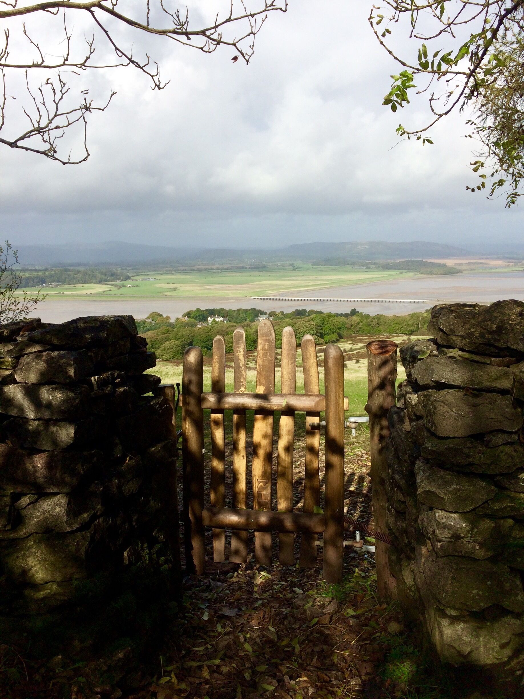 A stone archway leading to a view of a river, fields, and a bridge in the distance.