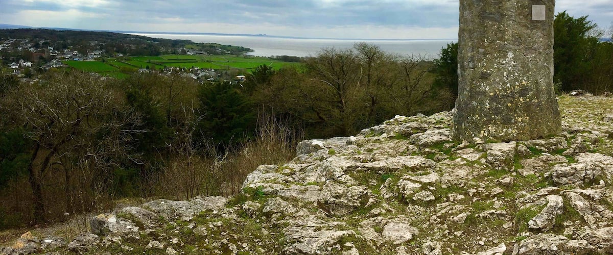 A stone tower on a rocky outcrop overlooking a coastal landscape with fields and a distant view of the sea.