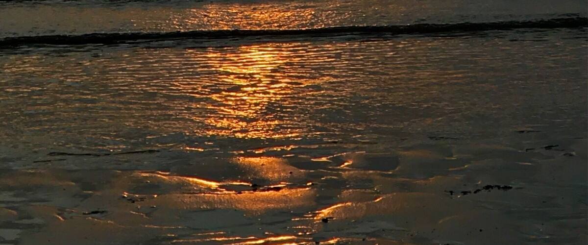 A sunset over a calm sea with two boats silhouetted against the sky.