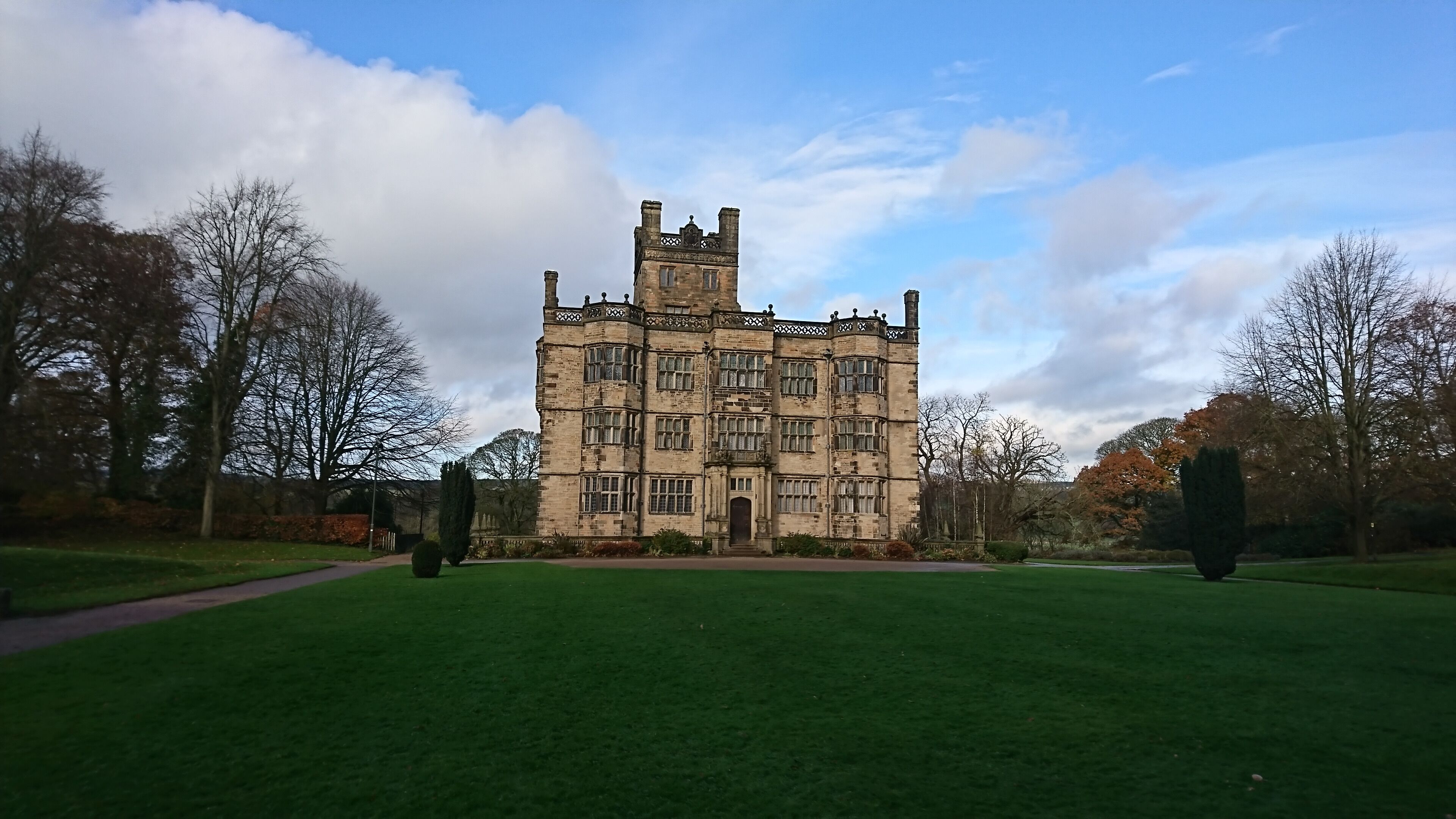 A large, historic stone building with multiple towers and windows, surrounded by a well-maintained lawn and trees.