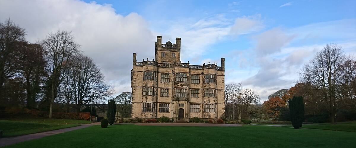 A large, historic stone building with multiple towers and windows, surrounded by a well-maintained lawn and trees.