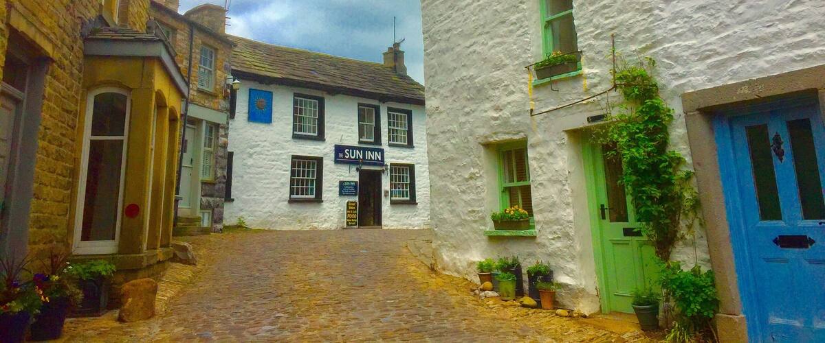 A cobblestone street with buildings, including a white building with a sign reading "The Sun Inn".