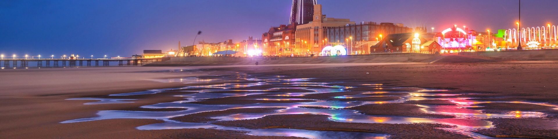 Uma praia com uma torre imponente e edifícios iluminados ao entardecer.