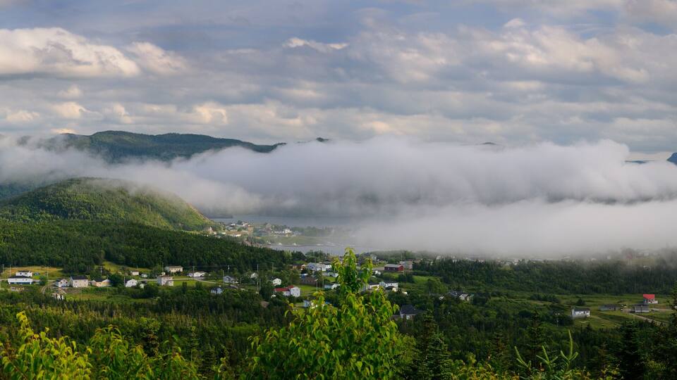 A coastal village surrounded by mountains and a lake, with dense forests and mist-covered peaks.