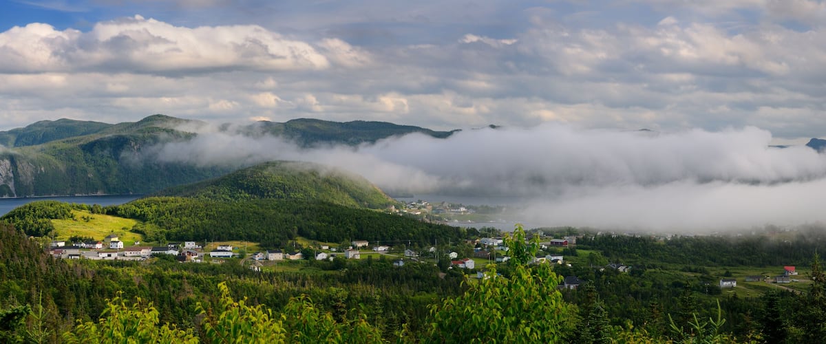 A coastal village surrounded by mountains and a lake, with dense forests and mist-covered peaks.