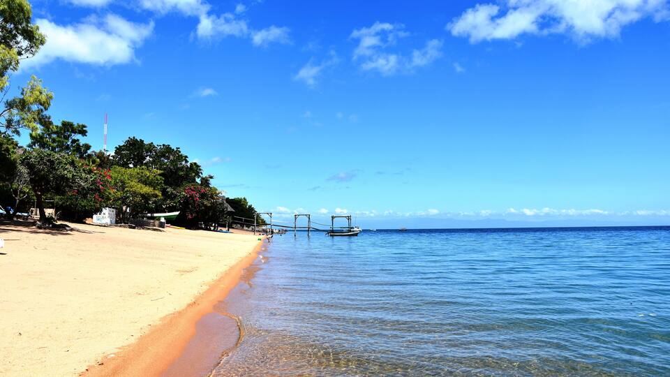 A beach with clear water, a sandy shore, and a bridge over the water.