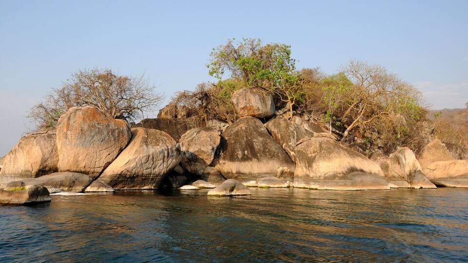 A rocky shoreline with large boulders and sparse vegetation.