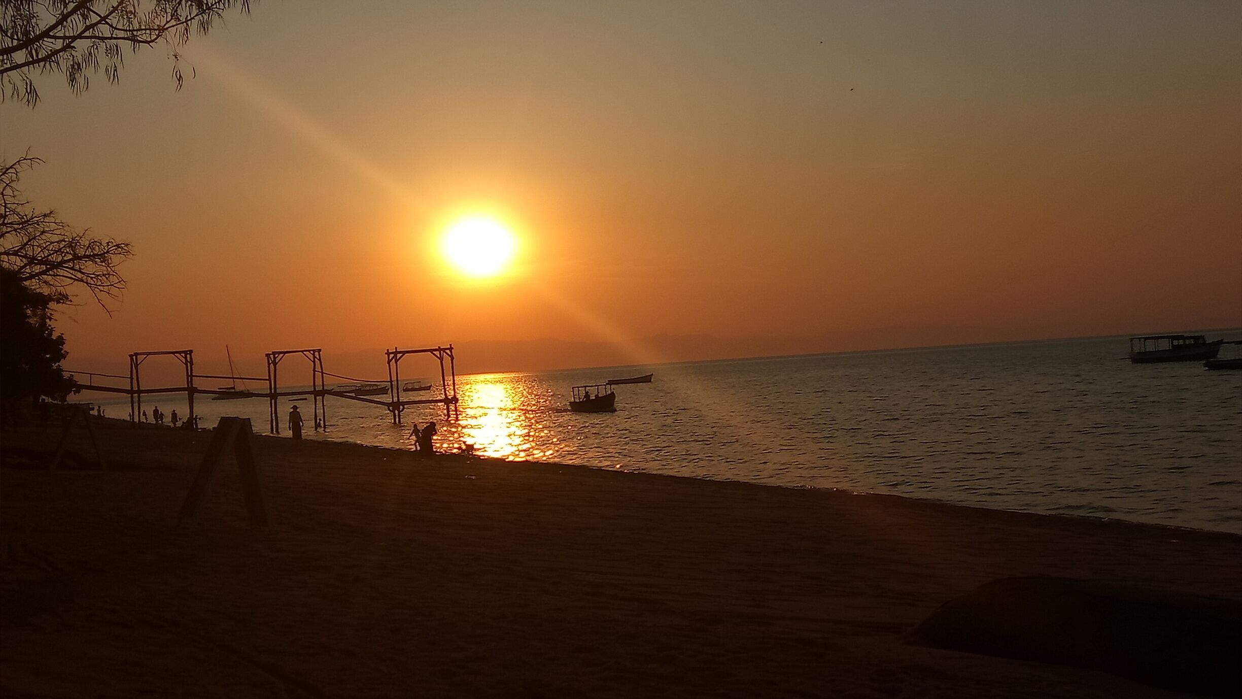 A sunset over a beach with a swing set and boats on the water.