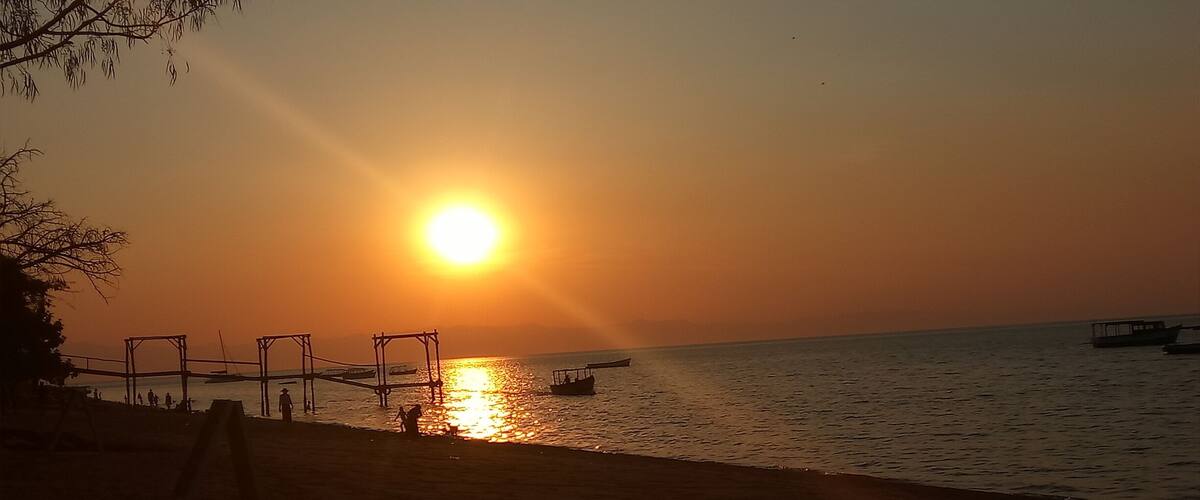 A sunset over a beach with a swing set and boats on the water.