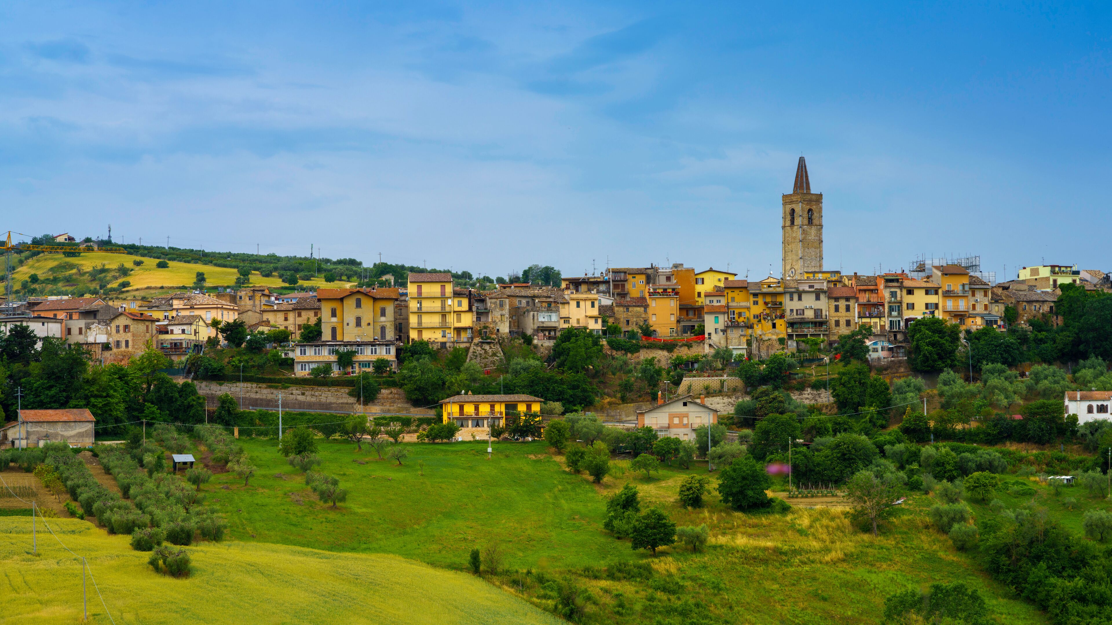A hillside town with colorful buildings, a prominent church tower, and lush green fields.