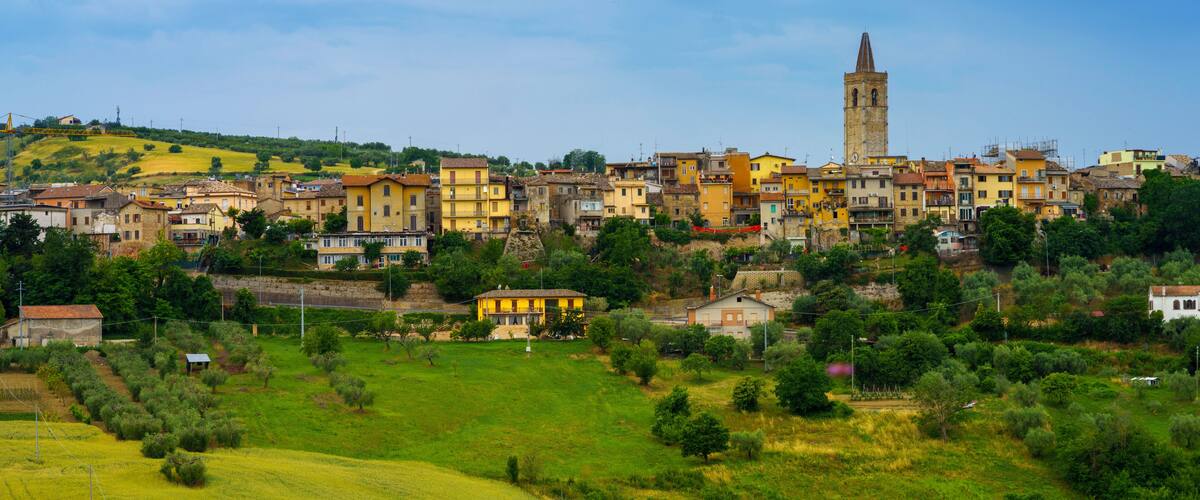 A hillside town with colorful buildings, a prominent church tower, and lush green fields.