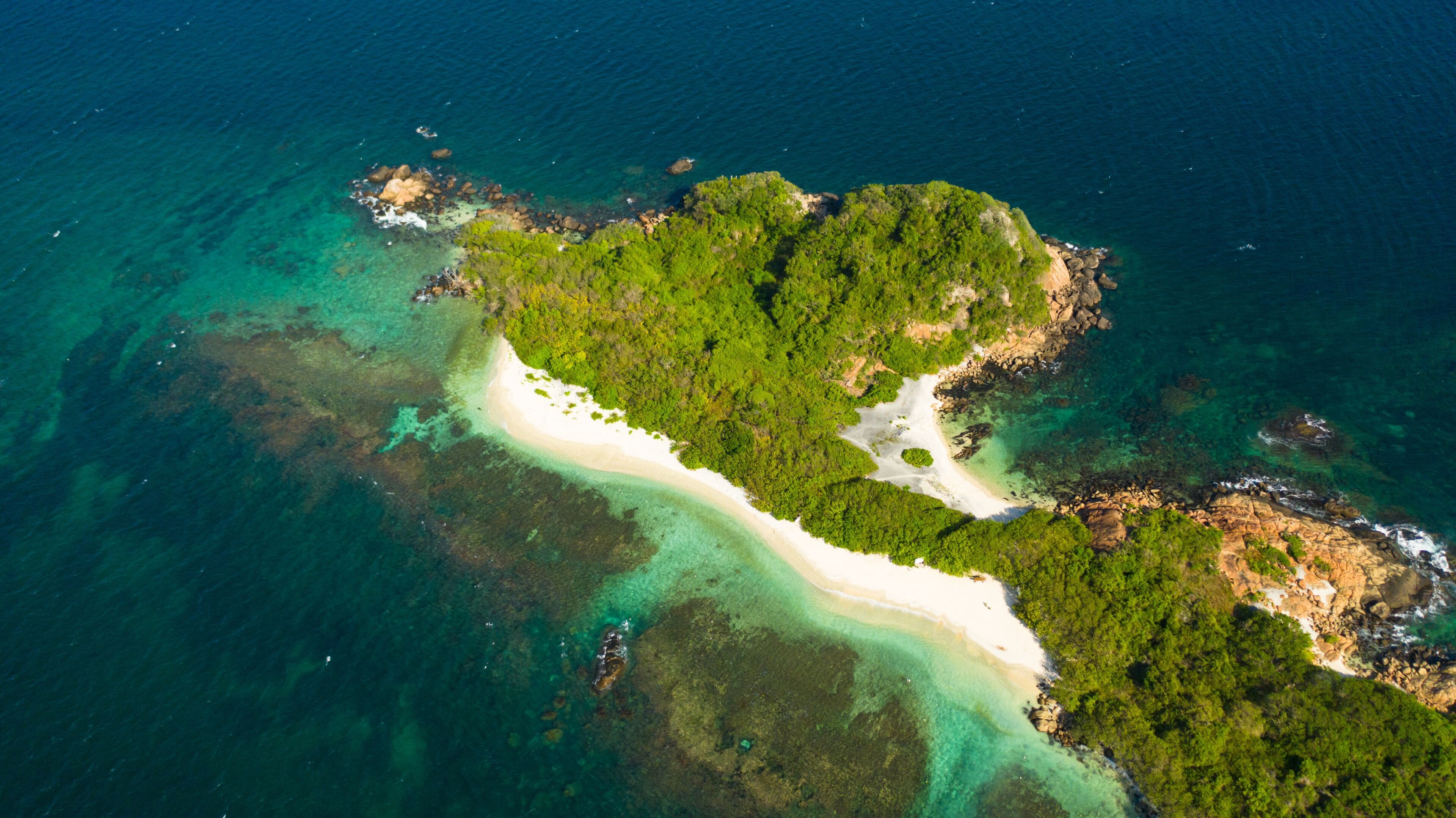 Vista aérea de una isla tropical con una playa de arena blanca, vegetación exuberante y aguas turquesas cristalinas.