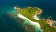An aerial view of a tropical island with a white sandy beach, lush green vegetation, and clear turquoise waters.