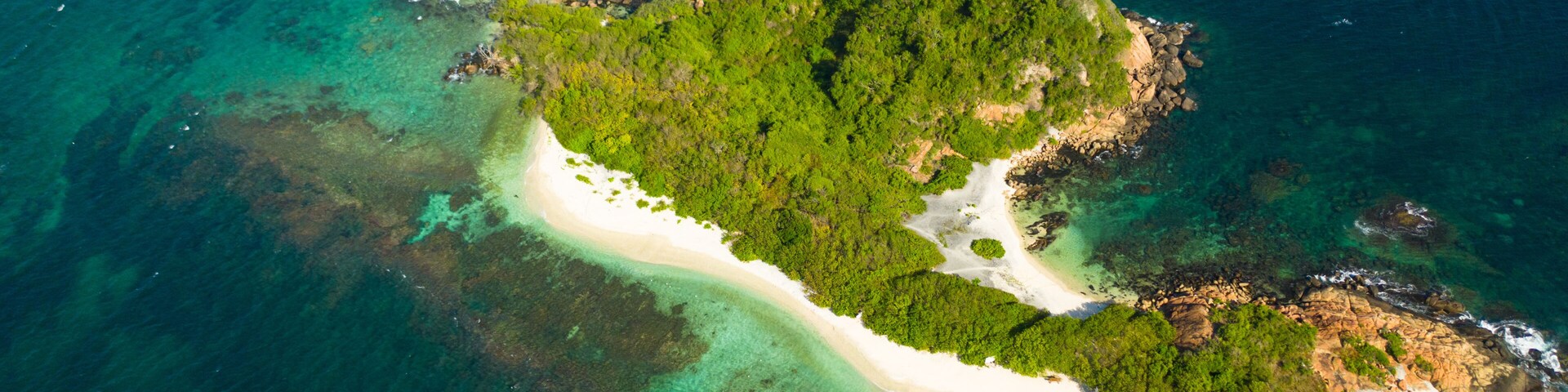 Vista aérea de una isla tropical con una playa de arena blanca, vegetación exuberante y aguas turquesas cristalinas.