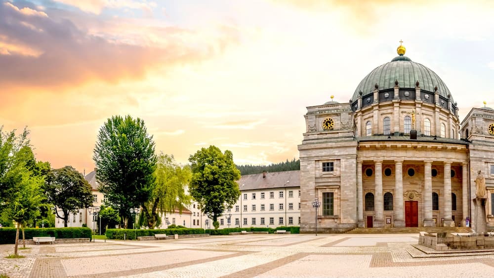 A historic building with a dome and columns, surrounded by a cobblestone square and trees.