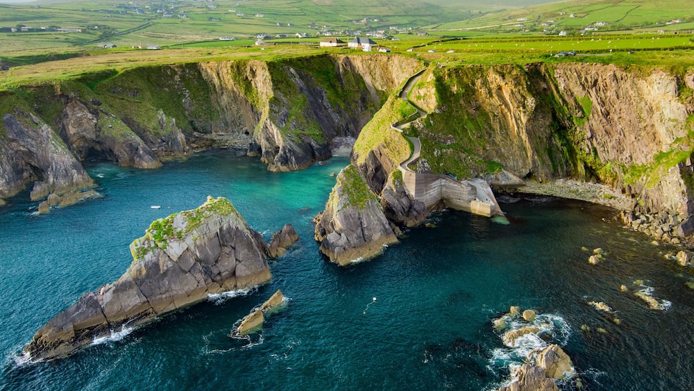 Dunquin or Dun Chaoin pier, Ireland's Sheep Highway. Aerial view of narrow pathway winding down to the pier, ocean coastline, cliffs. Popular location on Slea Head Drive and Wild Atlantic Way.