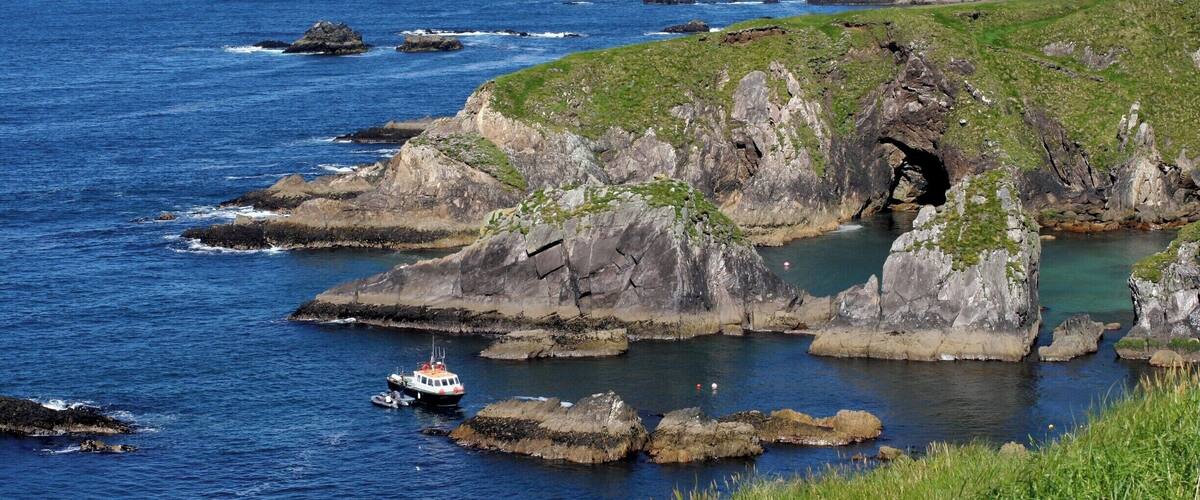 A coastal landscape with rocky cliffs, a boat, and a clear blue sea.