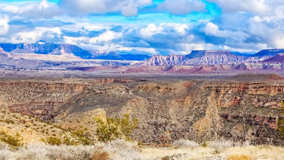 A vast canyon with layered rock formations and sparse vegetation.