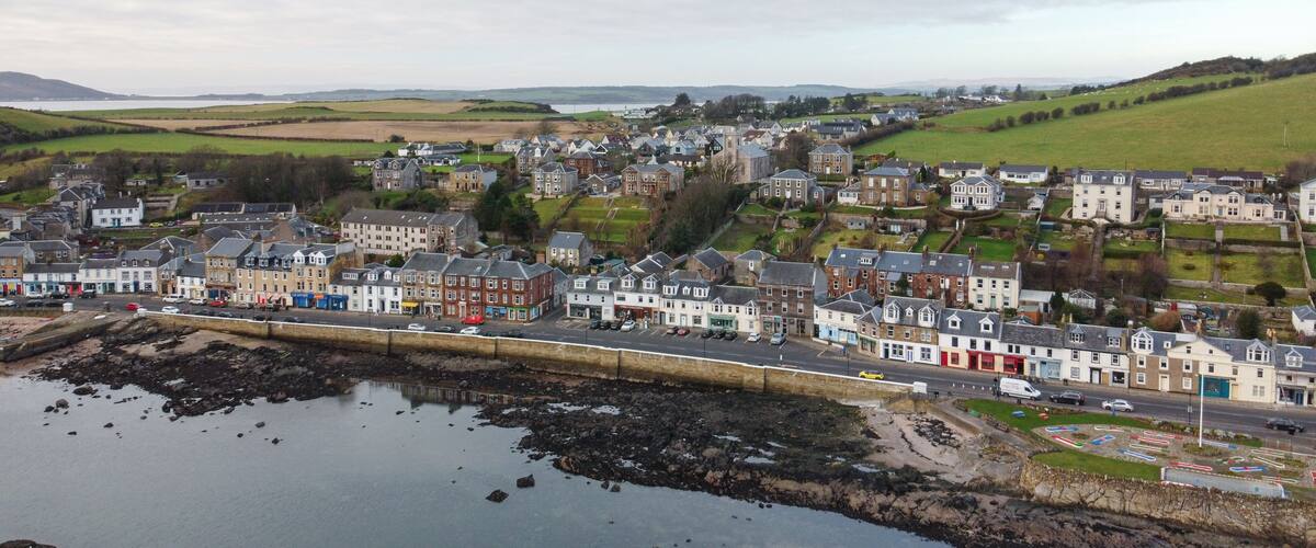 A coastal town with a mix of residential and commercial buildings, a rocky shoreline, and a large body of water.