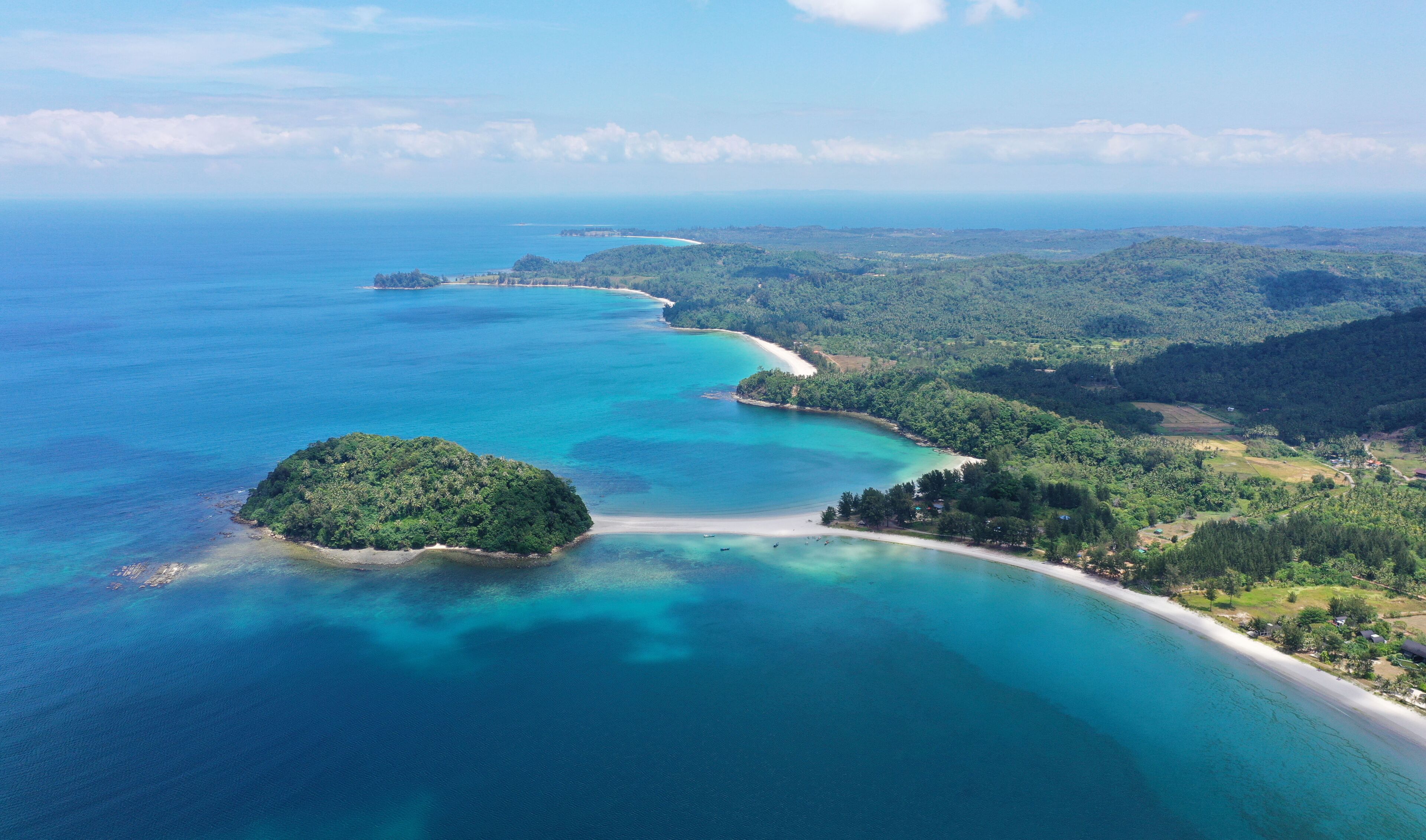 A coastal landscape with a clear turquoise sea, a sandy beach, and lush green hills.