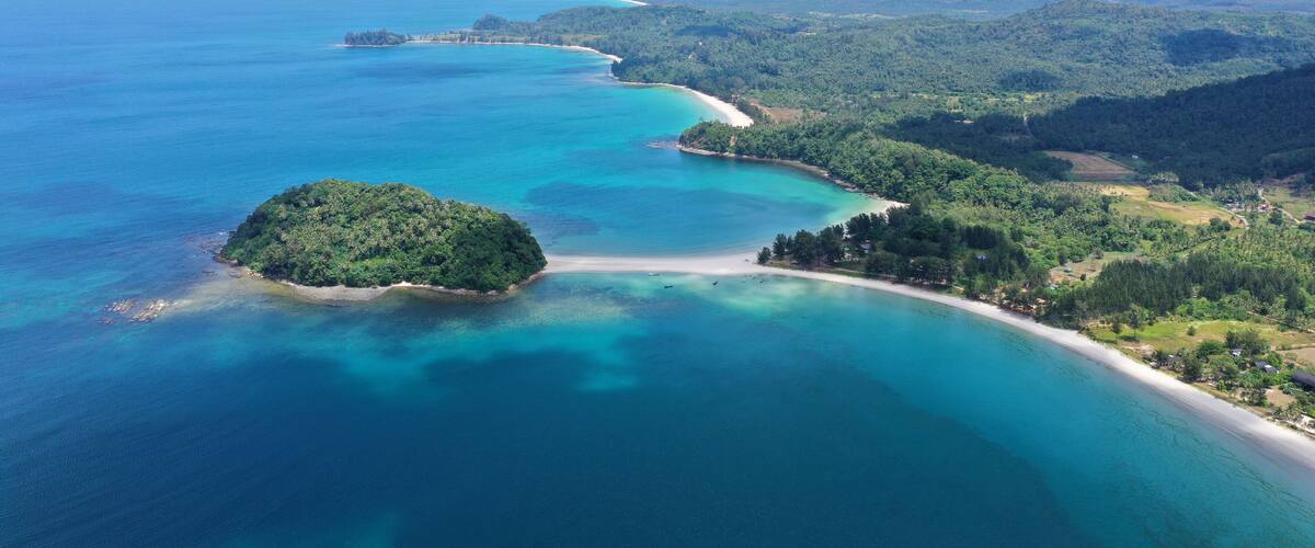 A coastal landscape with a clear turquoise sea, a sandy beach, and lush green hills.