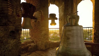 A bell tower with two large bells inside, a wooden floor, and a window with a view of the landscape.