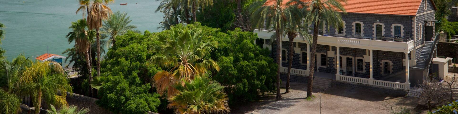 A coastal building with a red roof, surrounded by palm trees and a view of the sea.