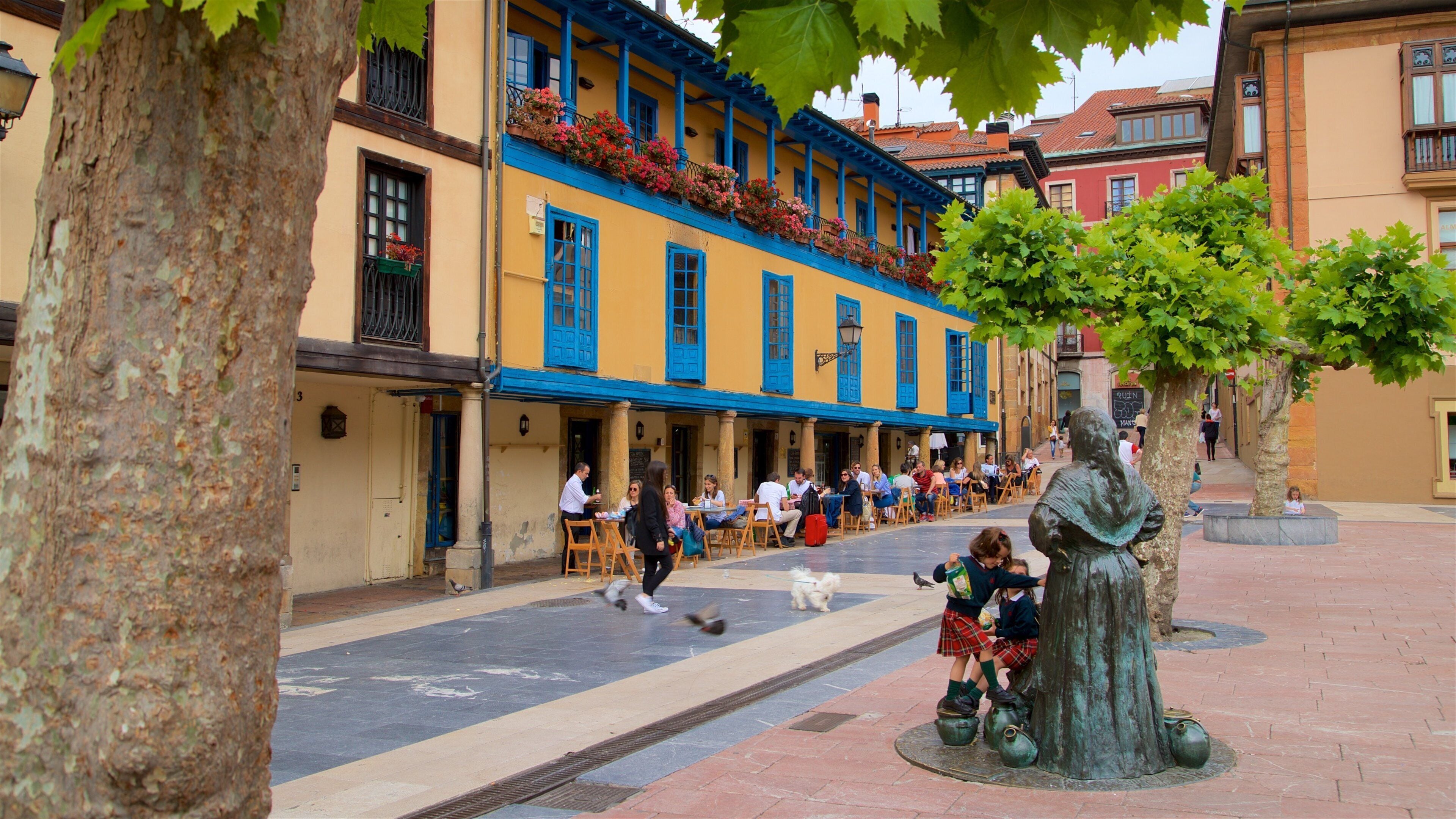 A plaza with colorful buildings, outdoor seating, and a statue.