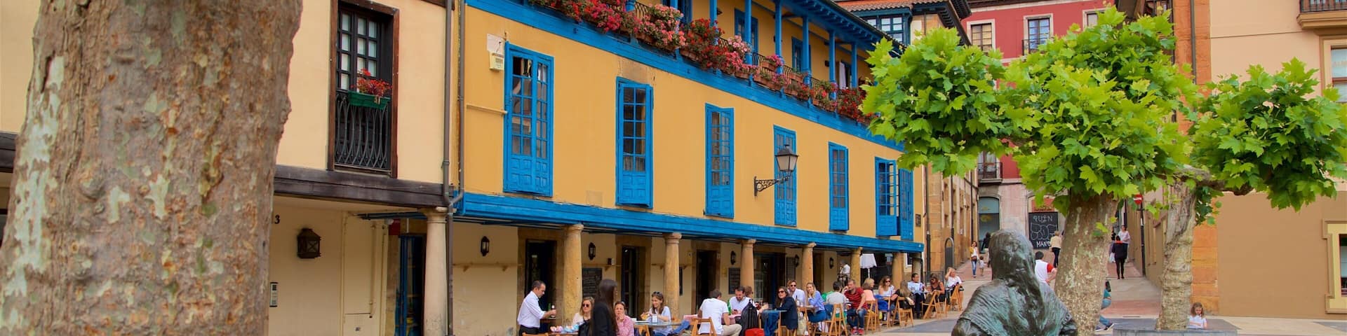 A plaza with colorful buildings, outdoor seating, and a statue.