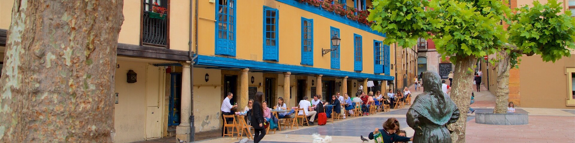 Uma praça com edifícios coloridos, mesas ao ar livre e uma estátua.