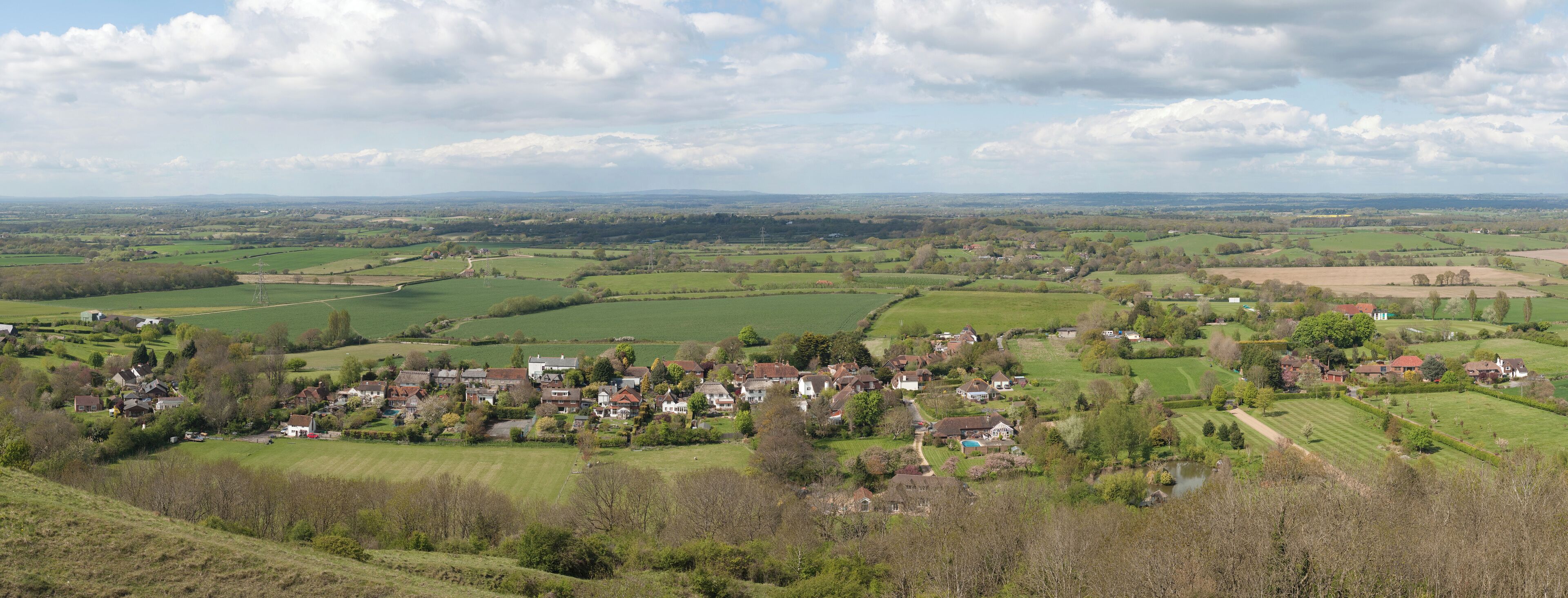 A rural landscape with rolling hills, a small village, and a distant power line tower.