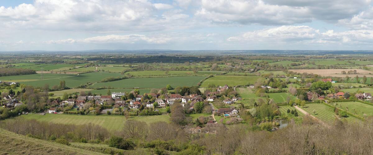 A rural landscape with rolling hills, a small village, and a distant power line tower.