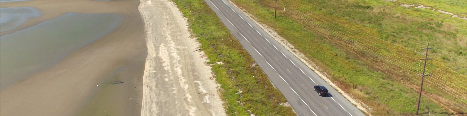 AERIAL: Black SUV car driving on countryside road along the Bay of Mexico