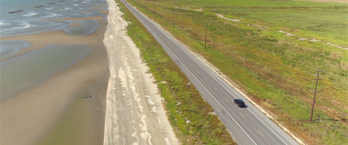 A coastal road with a beach on one side and open fields on the other.
