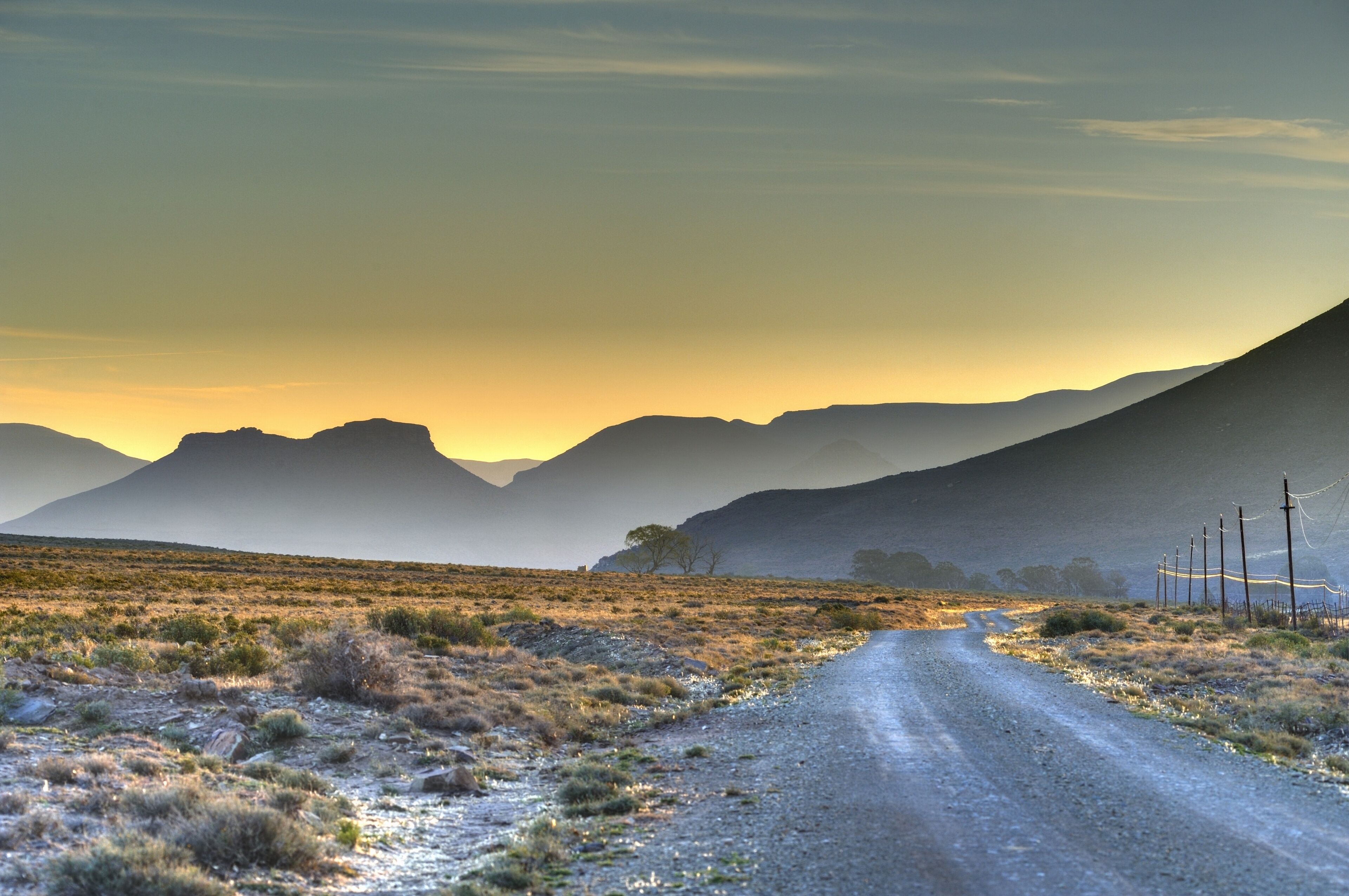 A dirt road in a desert landscape with mountains in the background.