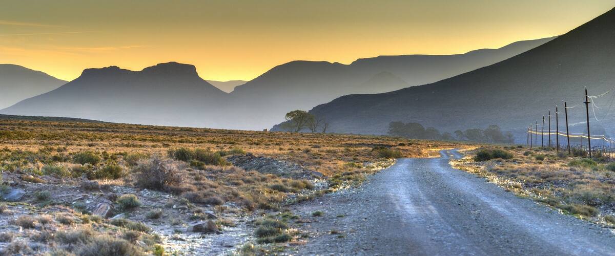 A dirt road in a desert landscape with mountains in the background.