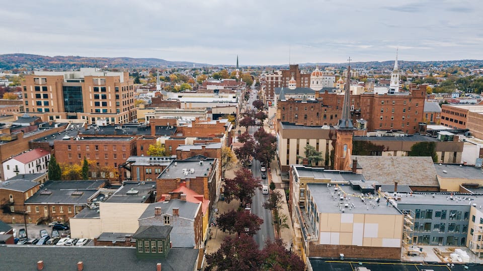 A cityscape with a mix of historic and modern buildings, a prominent church steeple, and a distant mountain range.