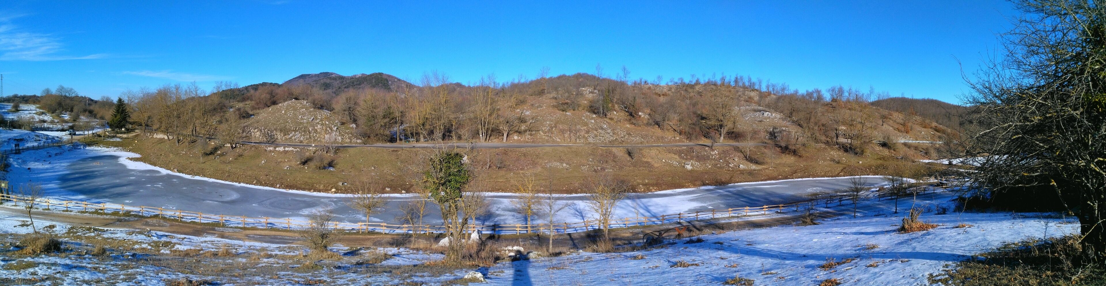 A snow-covered landscape with a winding road, a mountain in the background, and a clear blue sky.