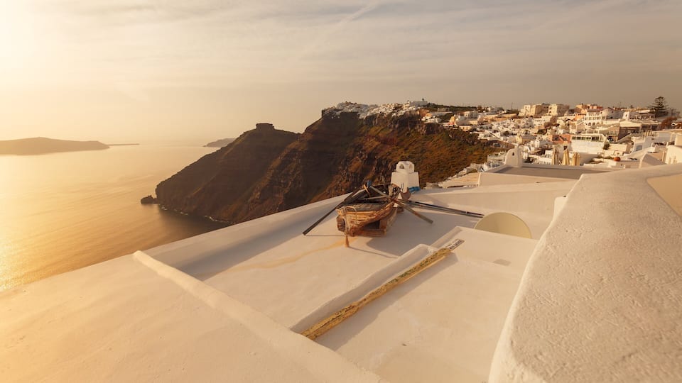 A coastal village with white buildings, a boat, and a cliff overlooking the sea.