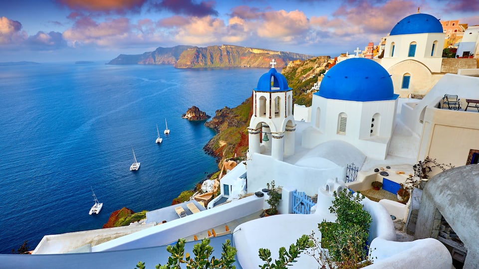 A coastal village with white buildings and blue domes, overlooking the sea with boats.