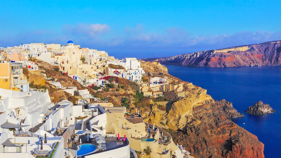 A coastal town with white buildings and blue domes, a cliff, and a body of water.