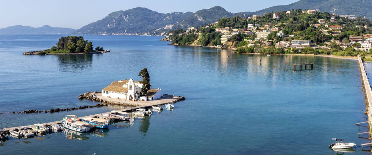 A coastal town with a marina, a small island with a church, and mountains in the background.