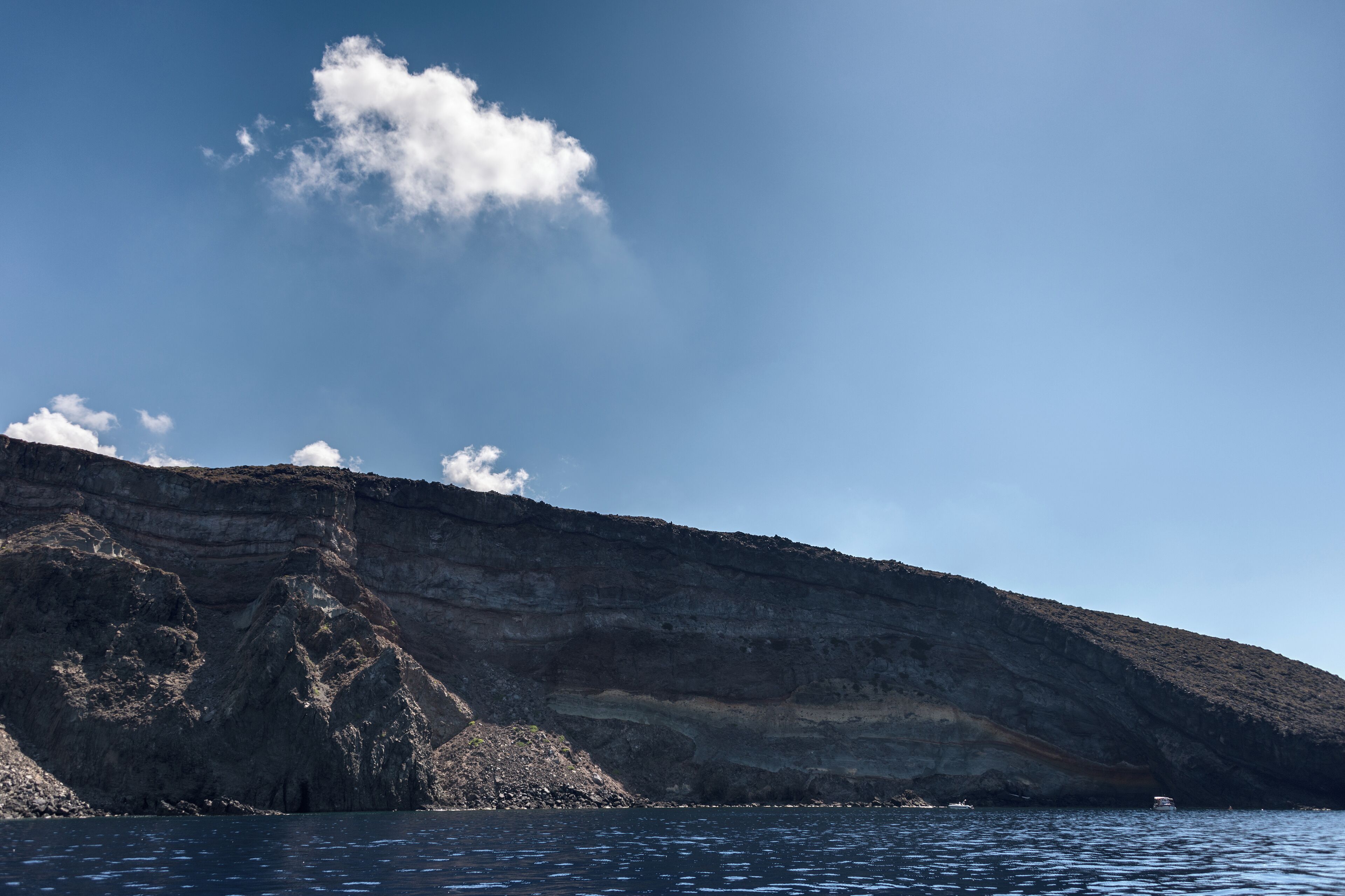 A coastal cliff with layered rock formations and a boat in the water.