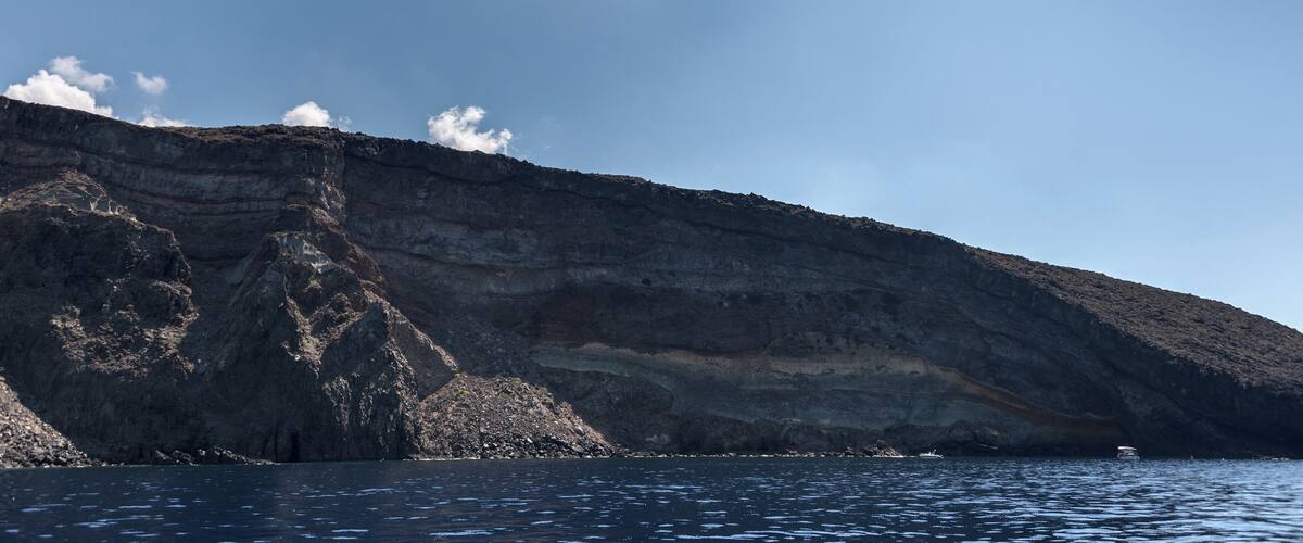A coastal cliff with layered rock formations and a boat in the water.