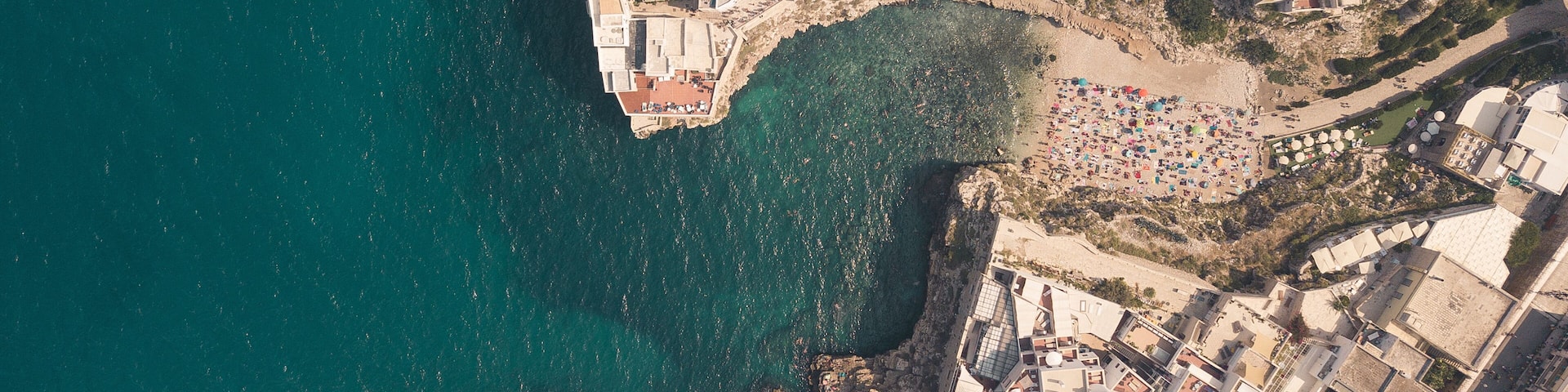 An aerial view of a coastal town with dense buildings, a beach, and a rocky coastline.