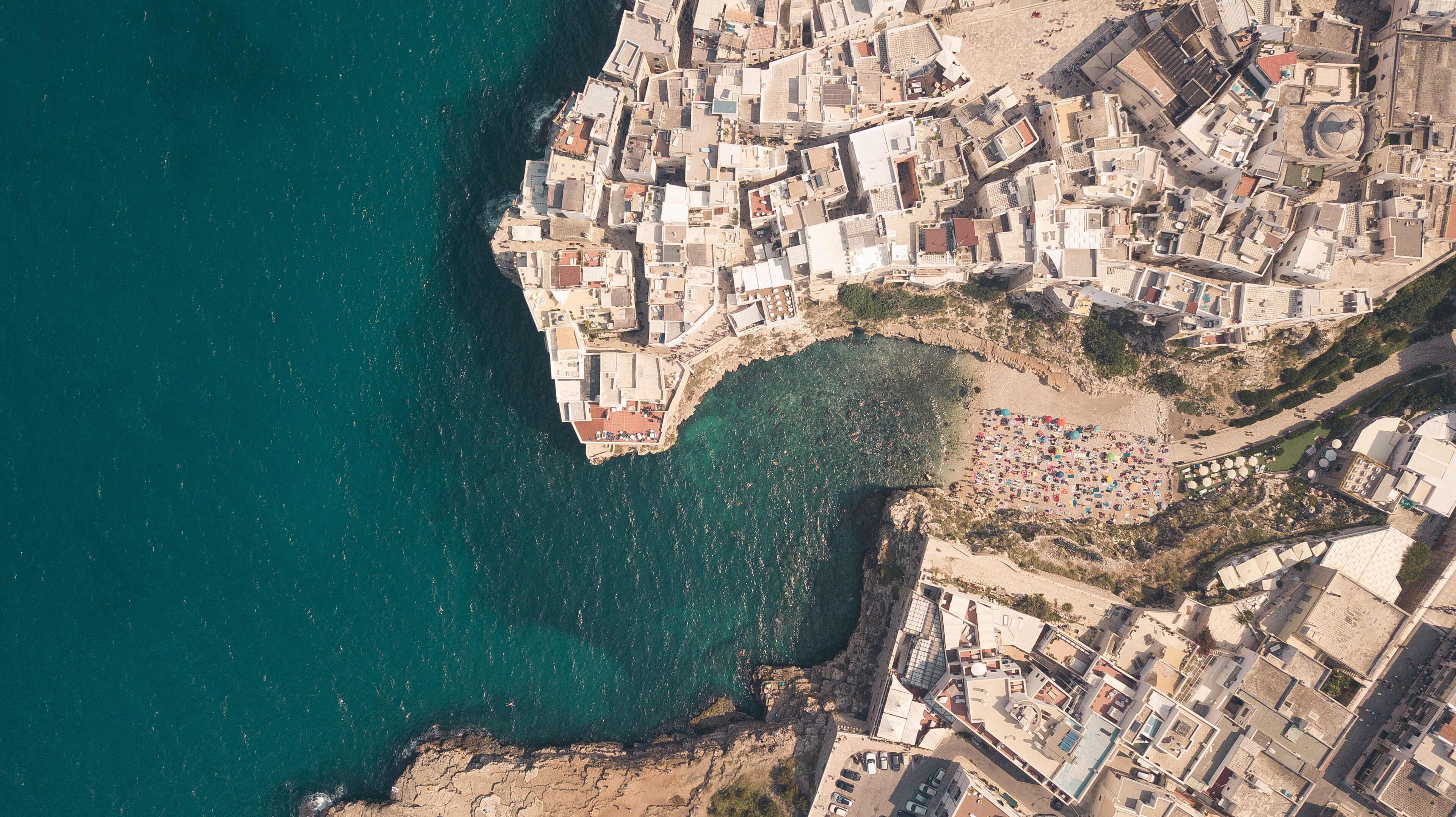 An aerial view of a coastal town with dense buildings, a beach, and a rocky coastline.