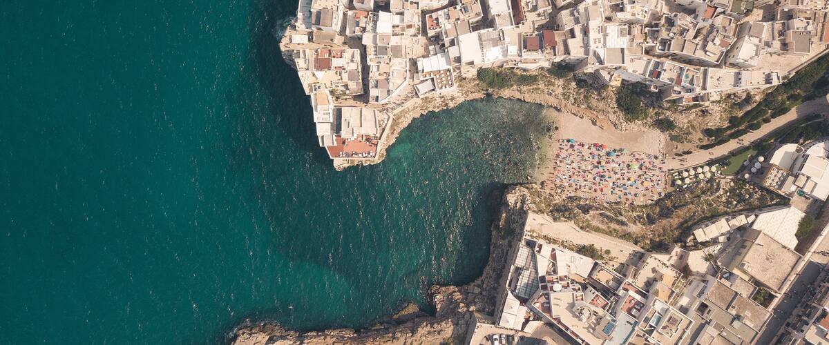 An aerial view of a coastal town with dense buildings, a beach, and a rocky coastline.