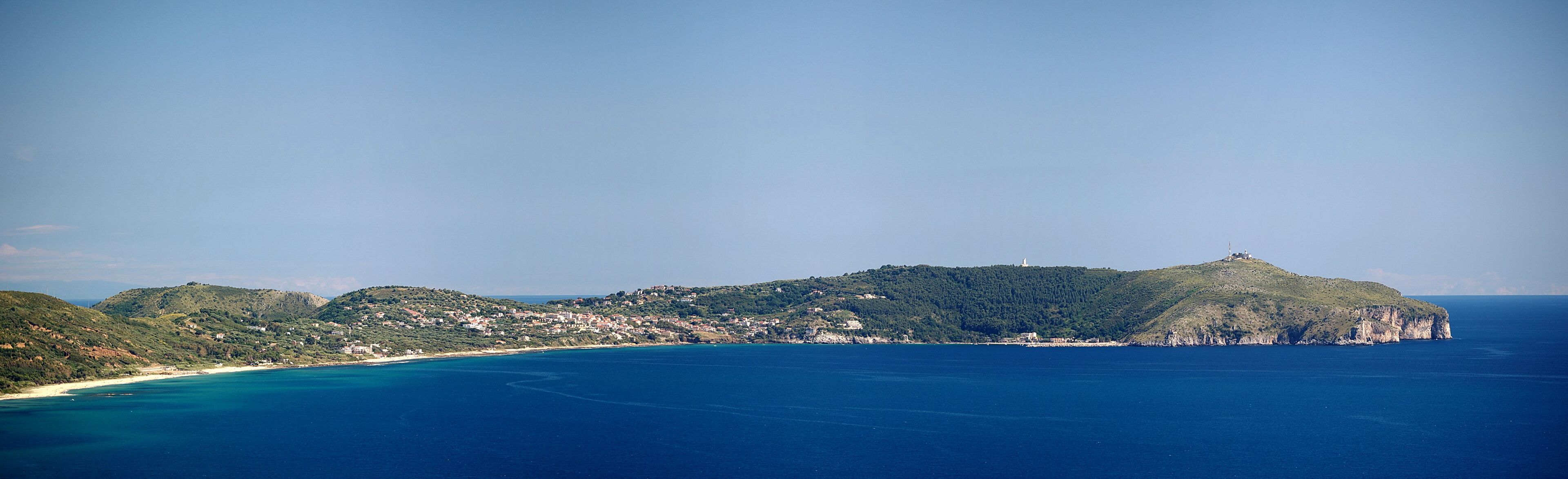 A coastal town with a lighthouse on a hill, surrounded by the sea and greenery.