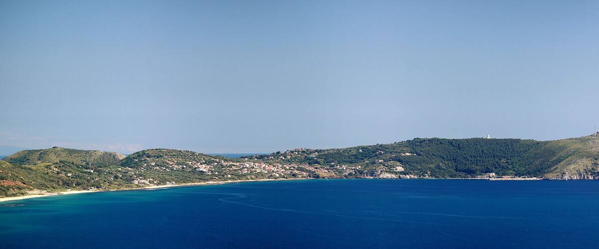 A coastal town with a lighthouse on a hill, surrounded by the sea and greenery.