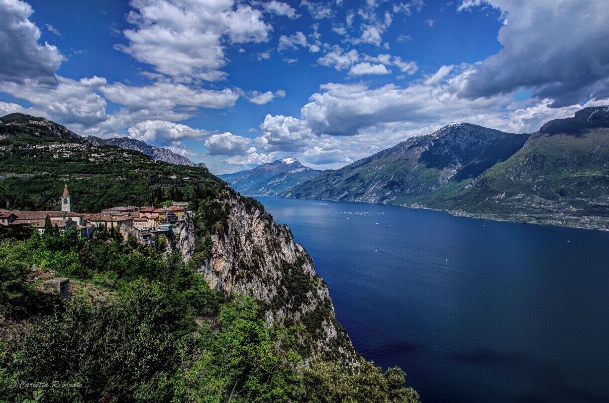 A coastal town with a church on a cliff overlooking a deep blue lake surrounded by mountains.